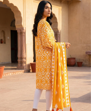 Woman in a yellow and white traditional outfit standing in front of a beige wall with arches.