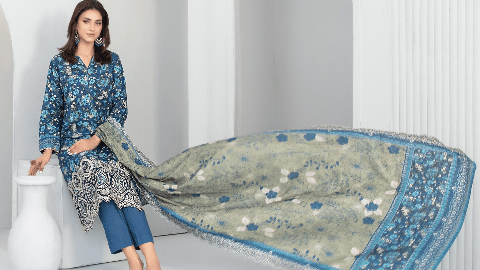 Woman holding a large fabric with intricate patterns in a minimalistic setting