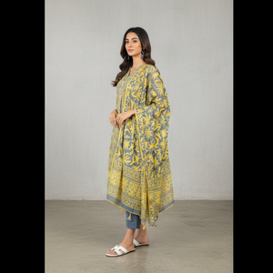 Woman wearing a yellow patterned dress with blue jeans against a plain background