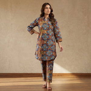 Woman wearing a patterned outfit standing in a well-lit room with wooden floor and beige wall.