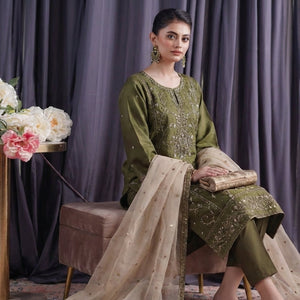 Woman in a green traditional outfit sitting in front of a floral arrangement with a purple curtain background