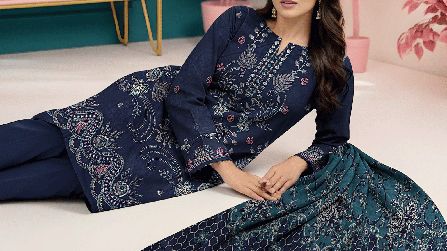 Woman in a blue patterned outfit sitting on a white floor with a pink dresser and plants in the background, featuring the brand 'Ayat'.