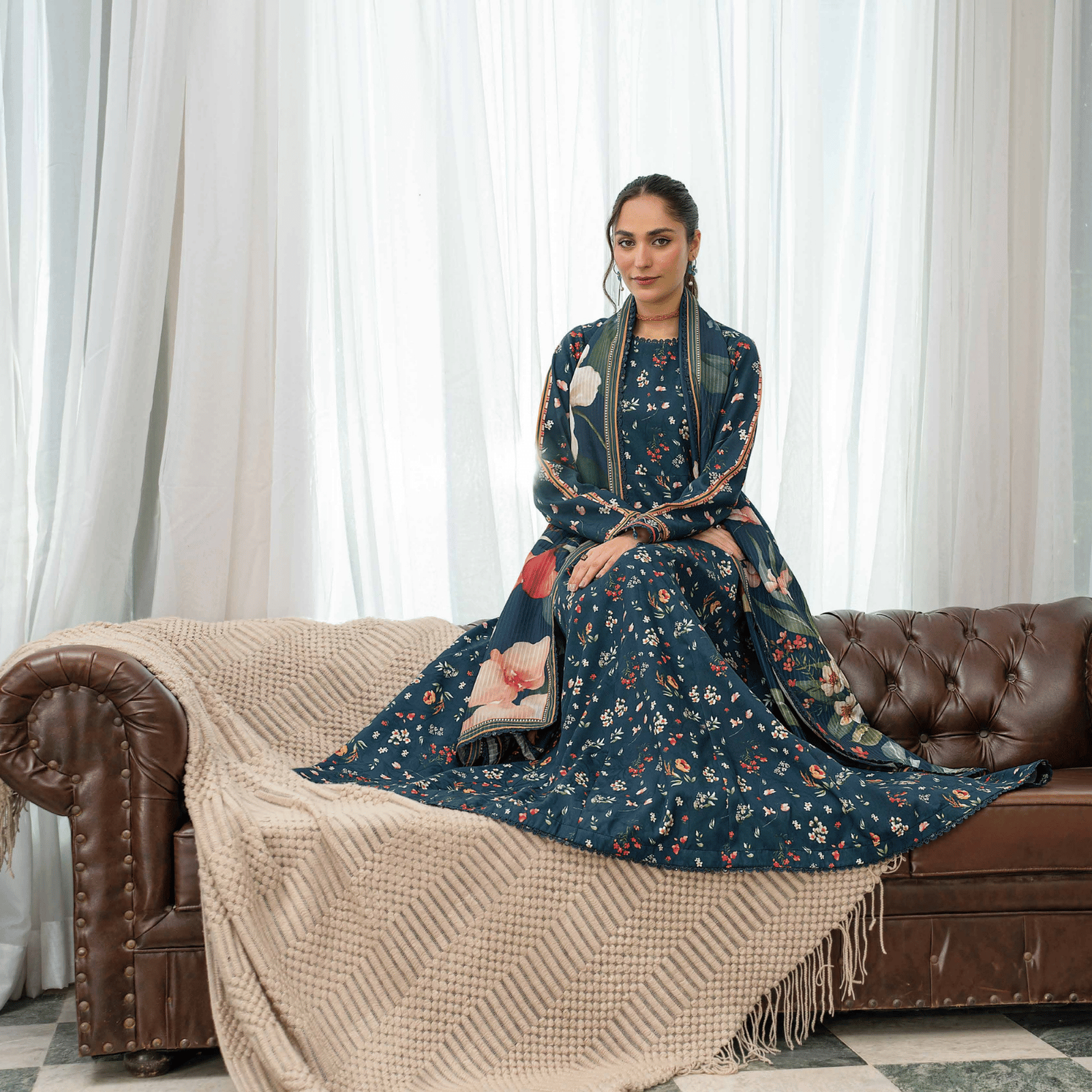 Woman in a floral dress sitting on a brown leather sofa in a decorated room.