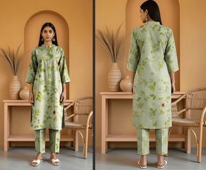 Woman wearing a green floral outfit standing in front of a mirror in a room with beige walls and wooden furniture.