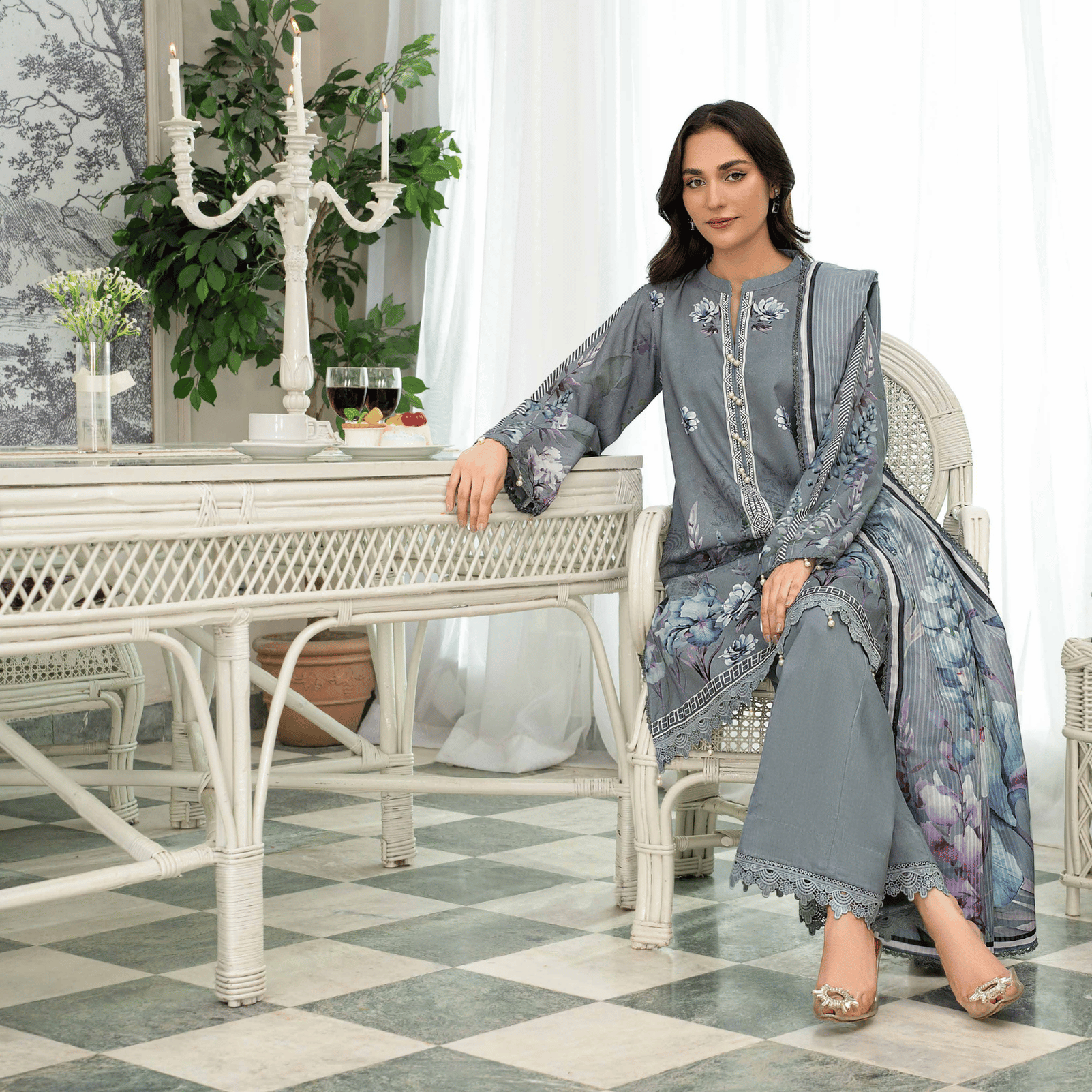 Woman in a gray and floral outfit sitting in a stylish room with white furniture and decor.