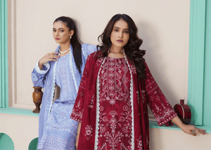 Two women in traditional outfits standing indoors with a light-colored wall and green window frames.