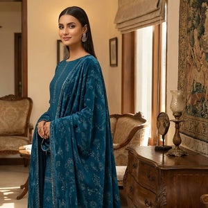 Woman in a blue traditional outfit standing in a decorated room with wooden furniture and tapestries.