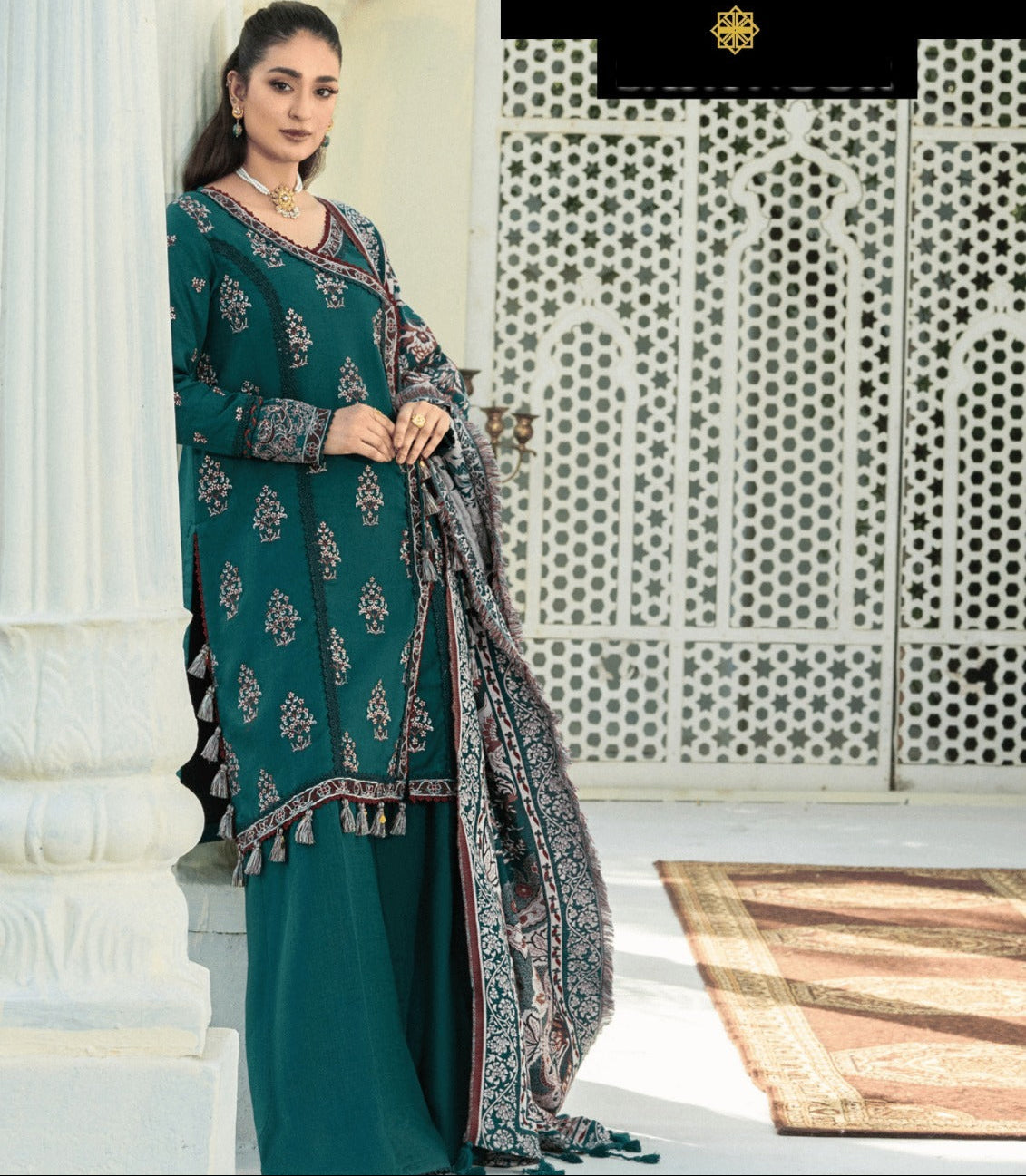 Woman in teal traditional outfit with patterned dupatta standing in front of a decorative wall, with 'Mehlab' brand visible.