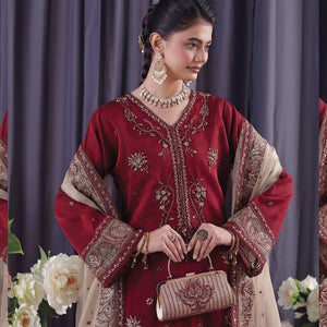Woman in a red and beige traditional outfit with floral decorations and a gray curtain background.