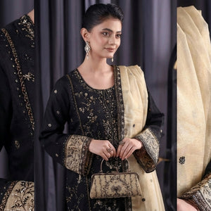 Woman in traditional black and gold outfit with a beige scarf, standing against a dark curtain.