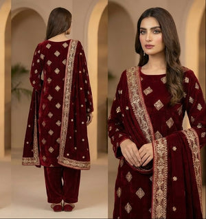 Woman modeling a maroon traditional outfit with gold embroidery in a neutral setting.