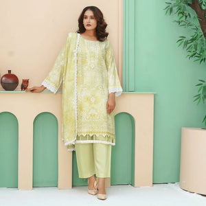 Woman in a light green traditional outfit standing in a decorated room with a plant and decorative items.